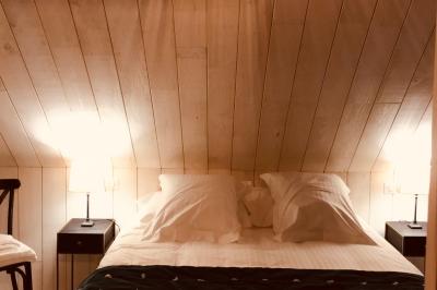 Lit double avec draps blancs, plaid bleu et tables de chevet avec lampes dans une chambre à la décoration rustique.