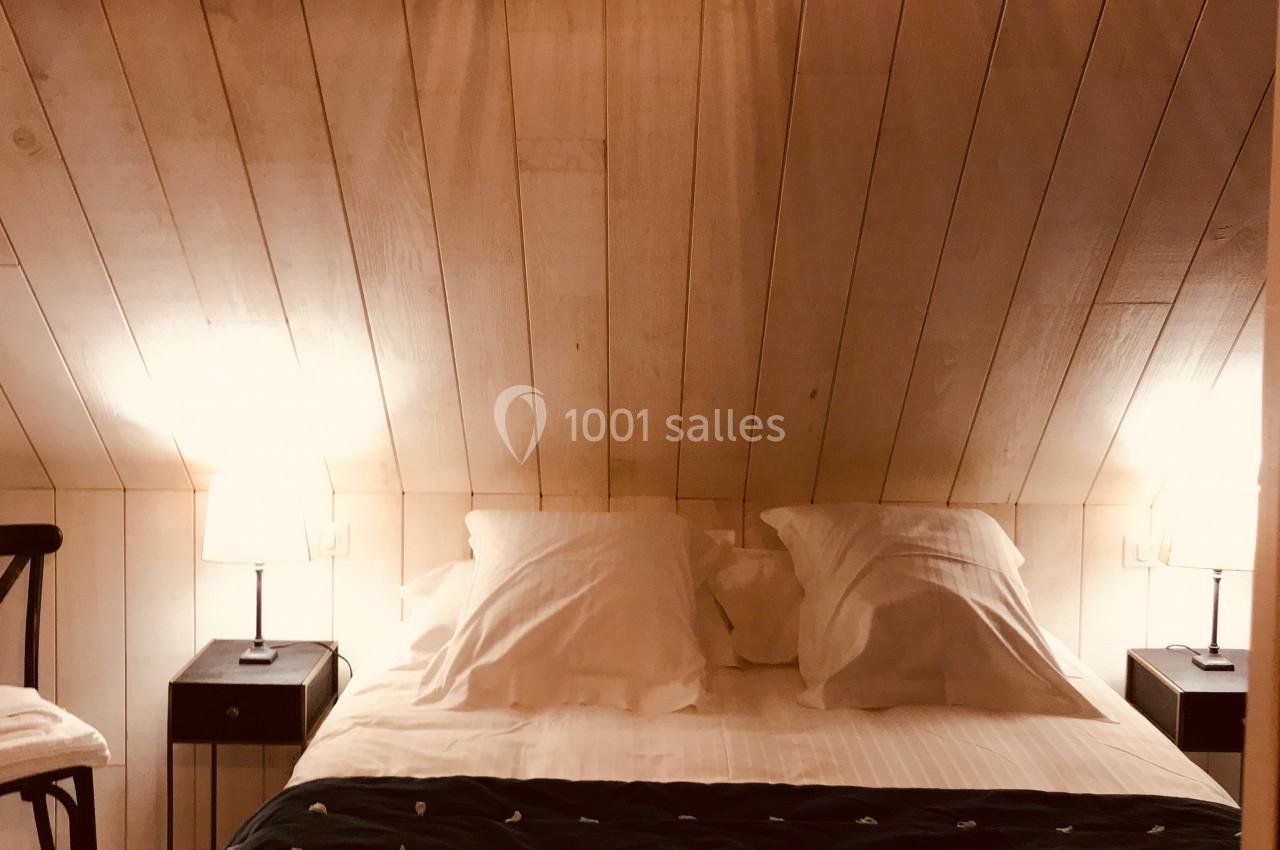 Lit double avec draps blancs et couverture sombre, encadré par deux lampes de chevet sur des tables noires, dans une pièce…