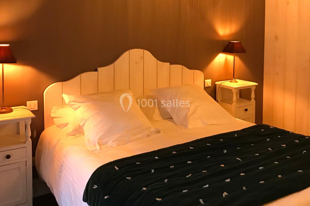 Lit double avec tête de lit en bois, couvert d'une couette sombre, entouré de tables de chevet et lampes allumées.