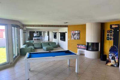 Vue d'un grand salon lumineux avec carrelage beige, cuisine ouverte et baies vitrées donnant sur un jardin.