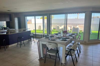 Vue d'un grand salon lumineux avec carrelage beige, cuisine ouverte et baies vitrées donnant sur un jardin.