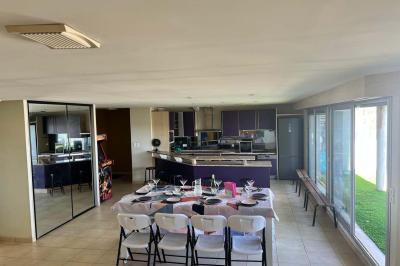 Vue d'un grand salon lumineux avec carrelage beige, cuisine ouverte et baies vitrées donnant sur un jardin.