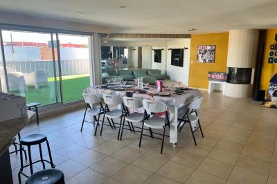 Vue d'un grand salon lumineux avec carrelage beige, cuisine ouverte et baies vitrées donnant sur un jardin.