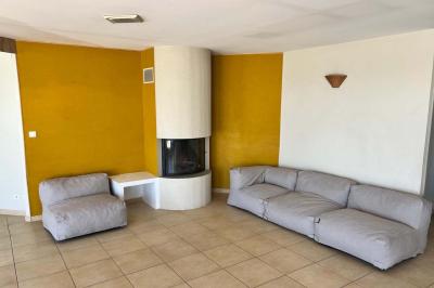 Vue d'un grand salon lumineux avec carrelage beige, cuisine ouverte et baies vitrées donnant sur un jardin.