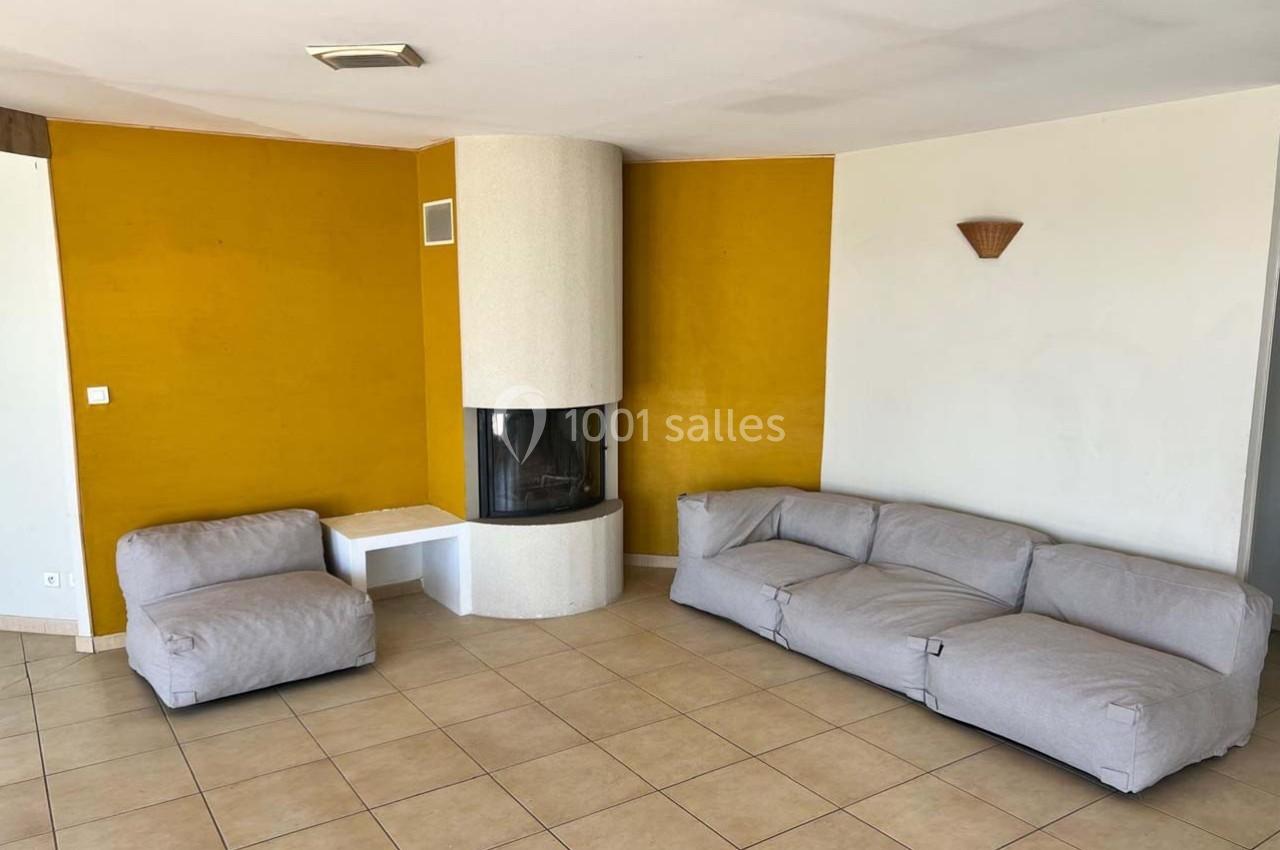 Salon avec murs jaunes, cheminée d'angle blanche, canapé gris en tissu et sol en carrelage beige.