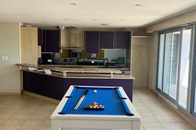 Vue d'un grand salon lumineux avec carrelage beige, cuisine ouverte et baies vitrées donnant sur un jardin.