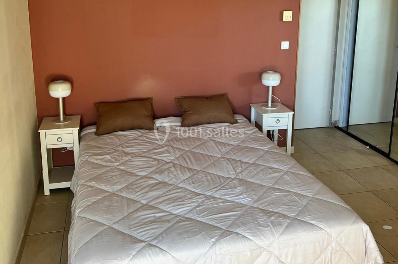 Lit double avec couette blanche, deux tables de chevet blanches avec lampes, mur rouge et placard à miroir.