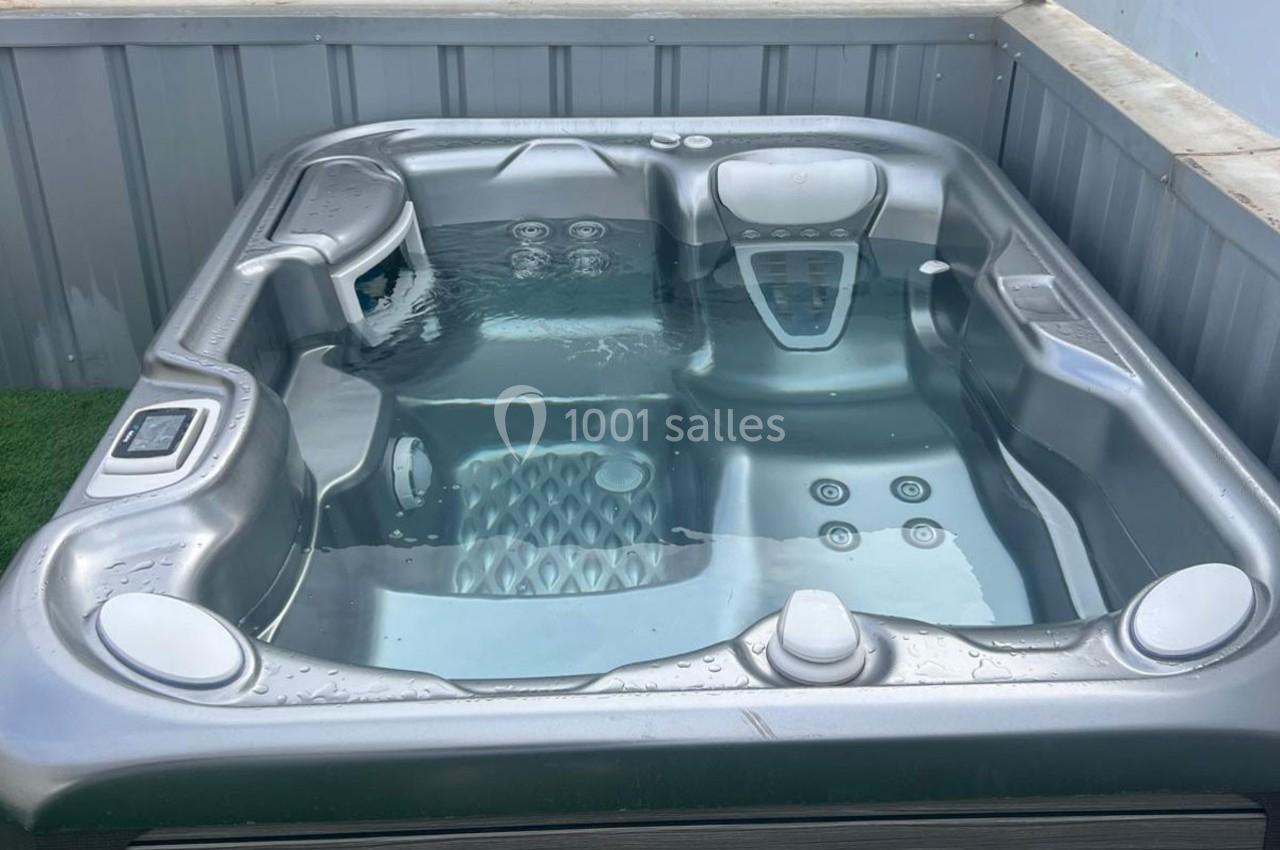 Bain à remous extérieur rempli d'eau, entouré de parois métalliques et posé sur une surface en gazon synthétique.