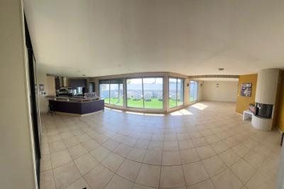 Vue d'un grand salon lumineux avec carrelage beige, cuisine ouverte et baies vitrées donnant sur un jardin.