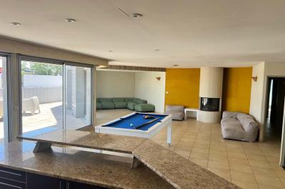 Grande pièce lumineuse avec carrelage beige, cuisine ouverte, baies vitrées donnant sur un jardin avec pelouse.