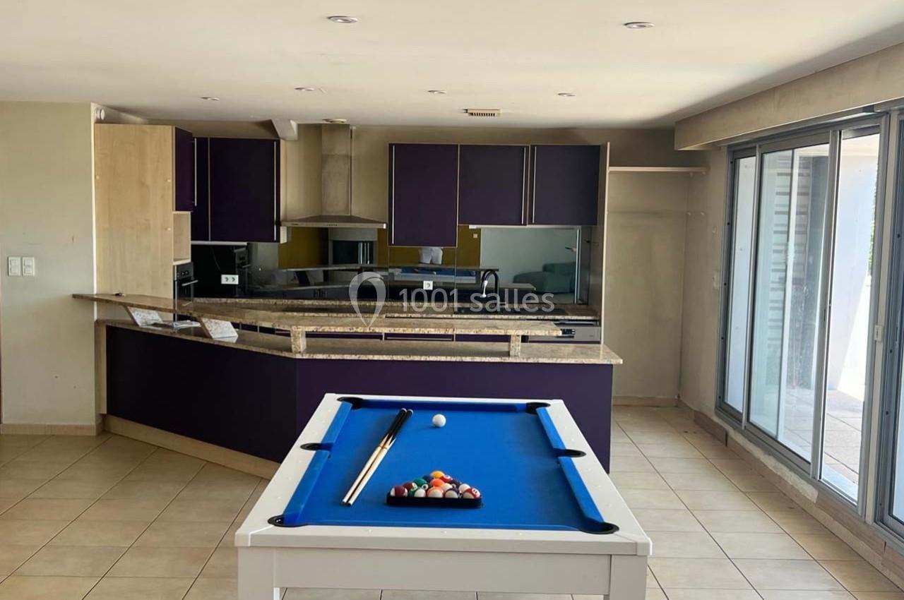 Cuisine moderne avec meubles violets, plan de travail en marbre, et table de billard blanche au premier plan.