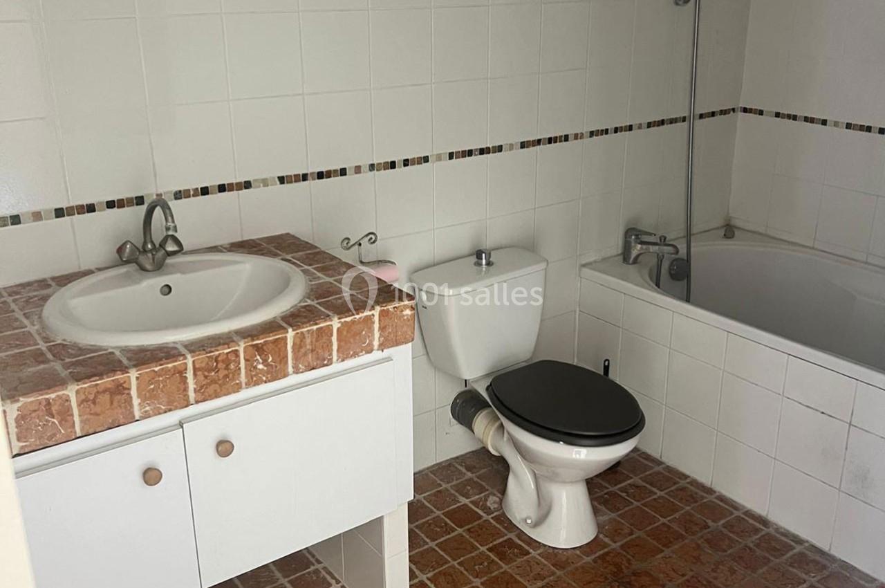 Salle de bain avec lavabo sur meuble en carrelage, toilettes, baignoire et murs carrelés blancs.
