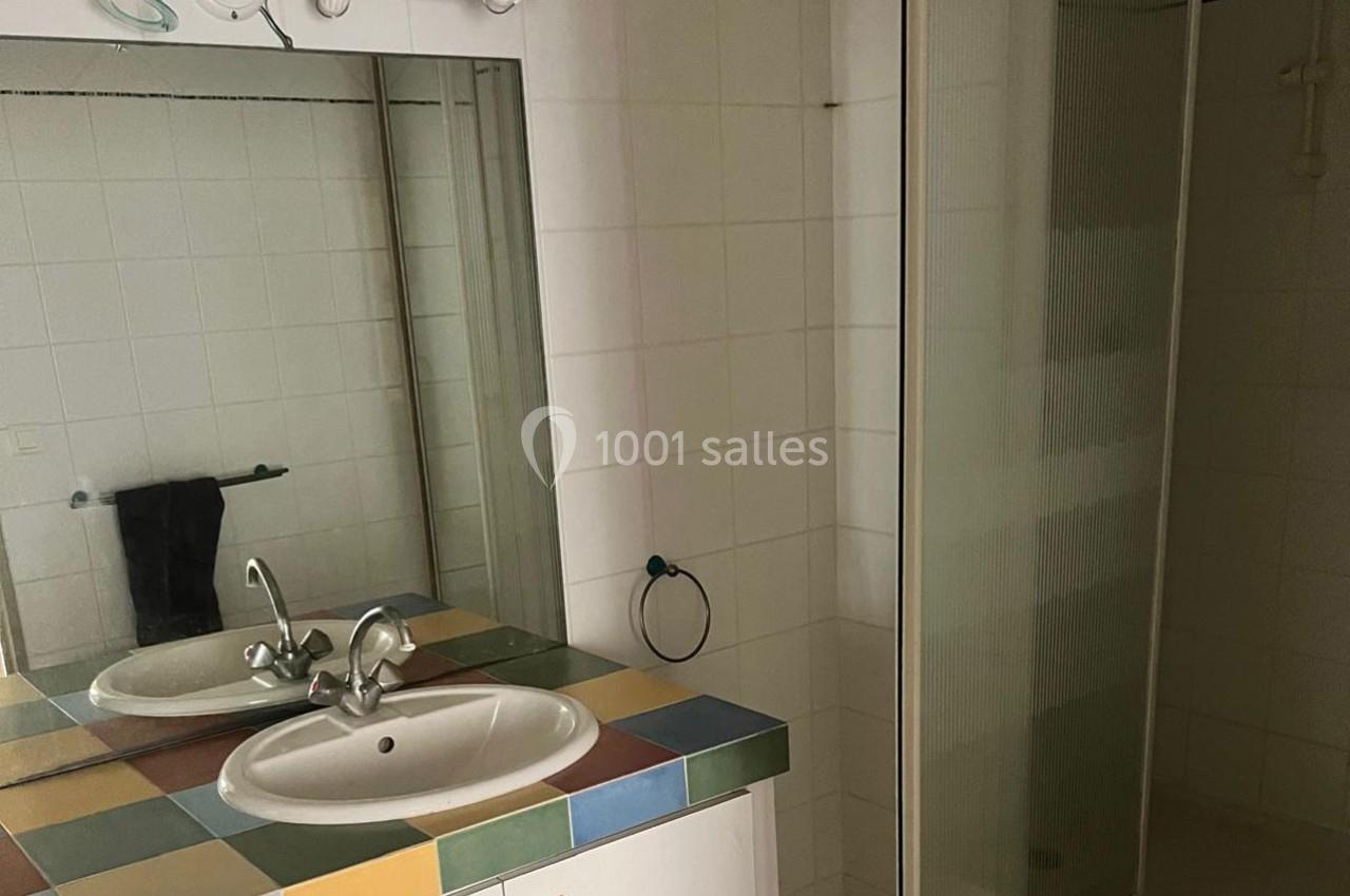 Salle de bain avec lavabo sur un plan de travail carrelé coloré, miroir, porte de douche vitrée et carrelage blanc.