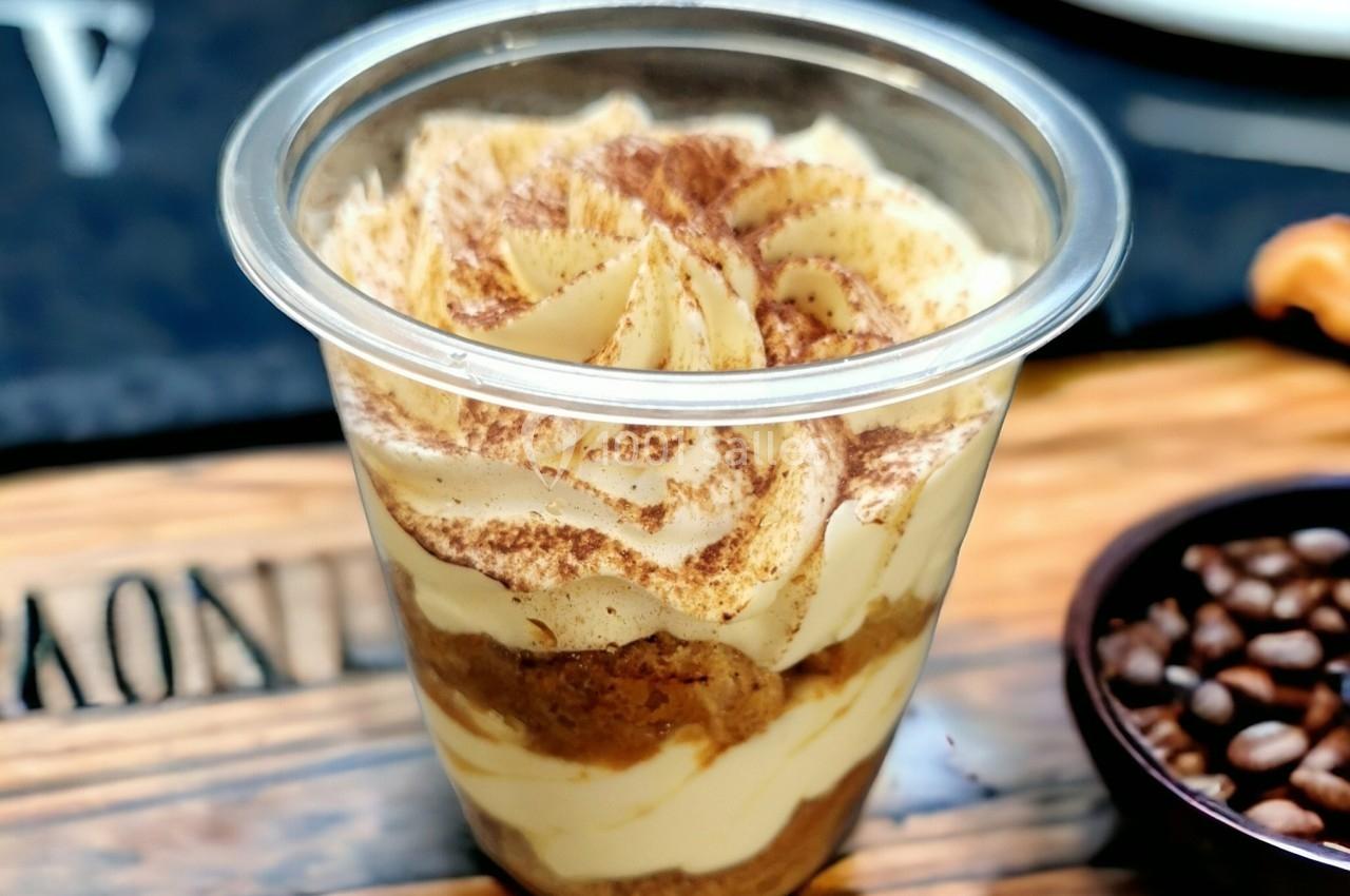 Dessert en verrine avec des couches de crème et de biscuit, saupoudré de cacao, posé sur une table en bois.