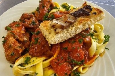 Assiette de tagliatelles fraîches avec sauce tomate, morceaux de viande, persil frais et croûton garni de lard grillé.
