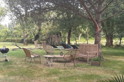 Maison en pierre entourée de verdure, avec un chemin de gravier, des arbres et un jardin en premier plan.