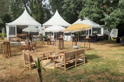 Maison en pierre entourée de verdure, avec un chemin de gravier, des arbres et un jardin en premier plan.
