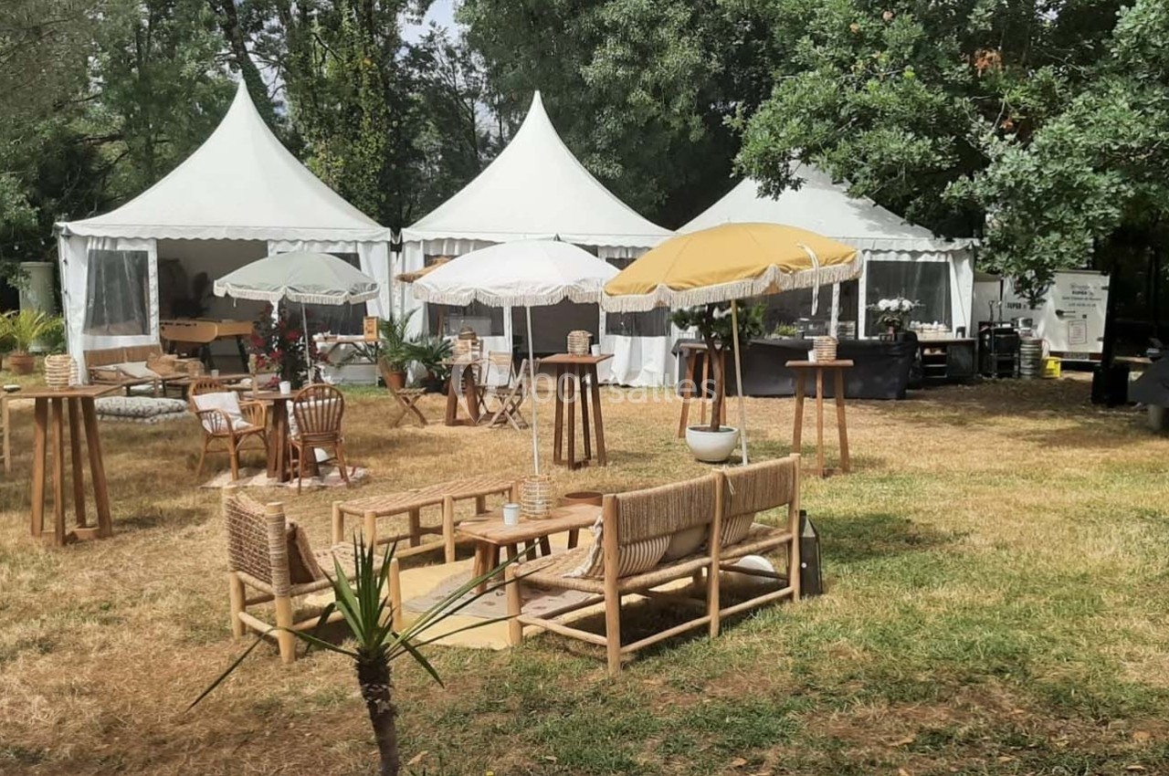 Mobilier en bois et parasols installés sur une pelouse devant des tentes blanches dans un cadre arboré.