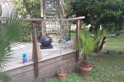 Maison en pierre entourée de verdure, avec un chemin de gravier, des arbres et un jardin en premier plan.