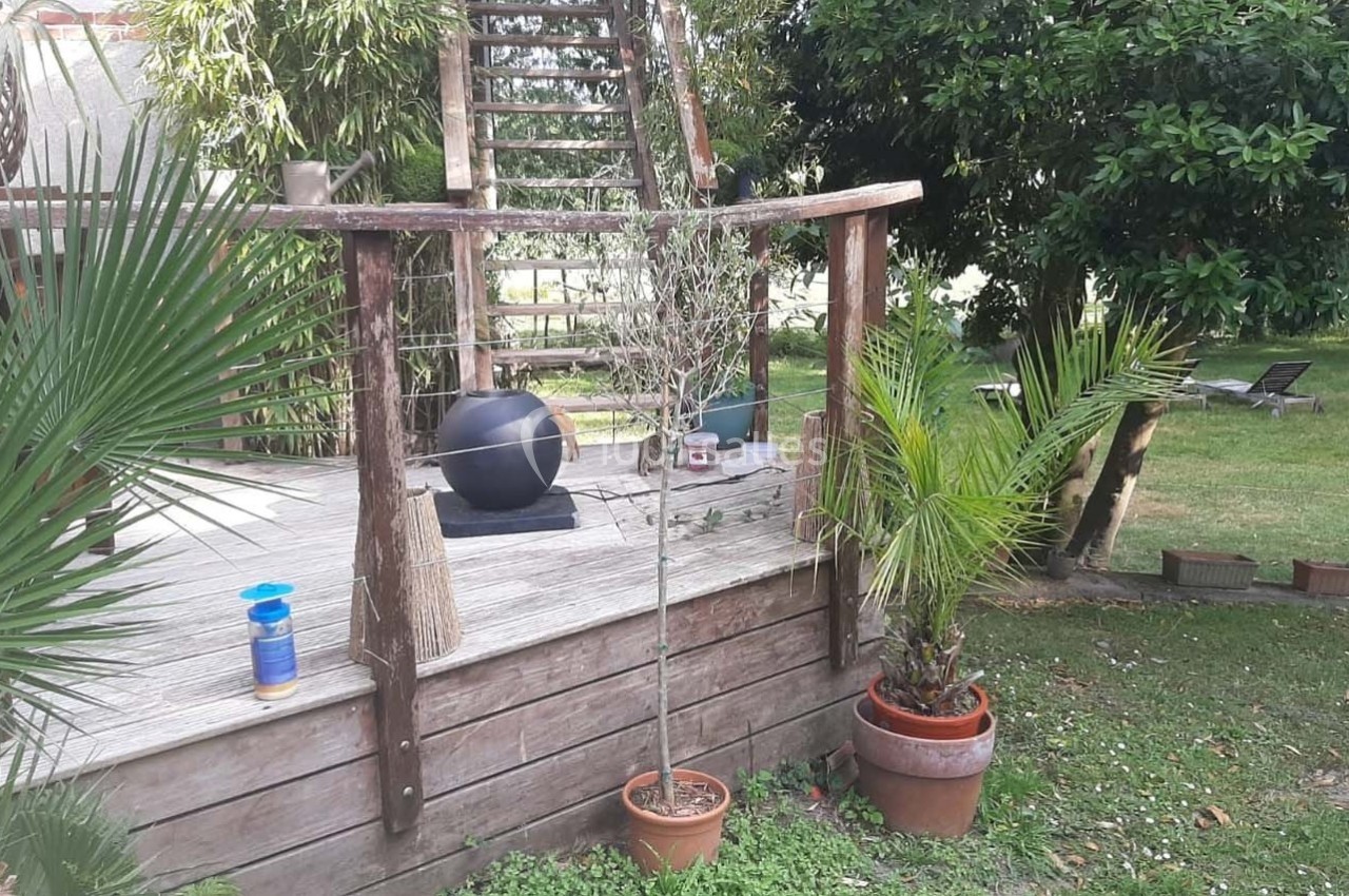 Terrasse en bois avec plantes en pot, balustrade en bois, ballon noir et jardin verdoyant en arrière-plan.