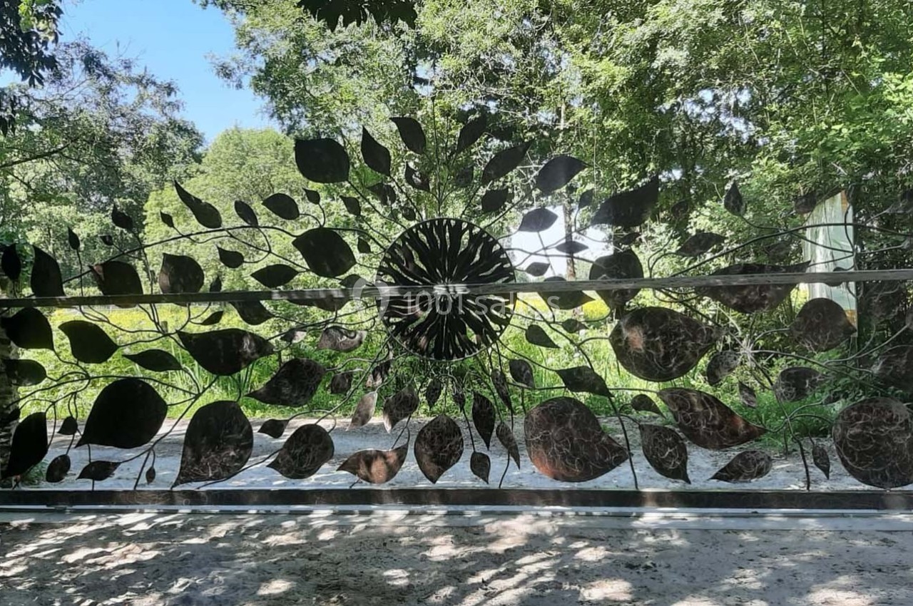 Portail métallique décoratif avec motifs de feuilles et de branches, entouré de végétation verdoyante.