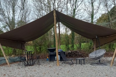 Maison en pierre entourée de verdure, avec un chemin de gravier, des arbres et un jardin en premier plan.