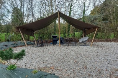 Maison en pierre entourée de verdure, avec un chemin de gravier, des arbres et un jardin en premier plan.