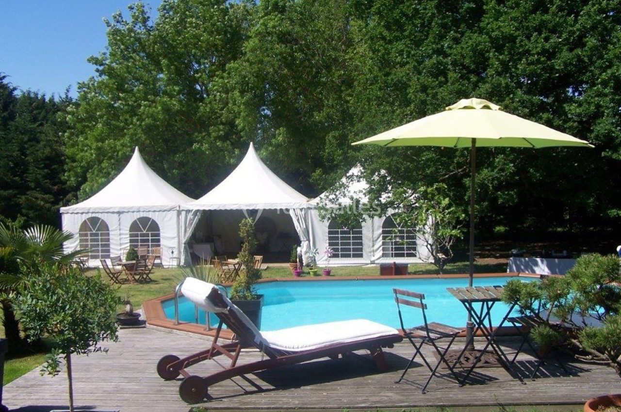 Piscine extérieure avec transat, parasol, terrasse en bois et tentes blanches dans un jardin arboré.