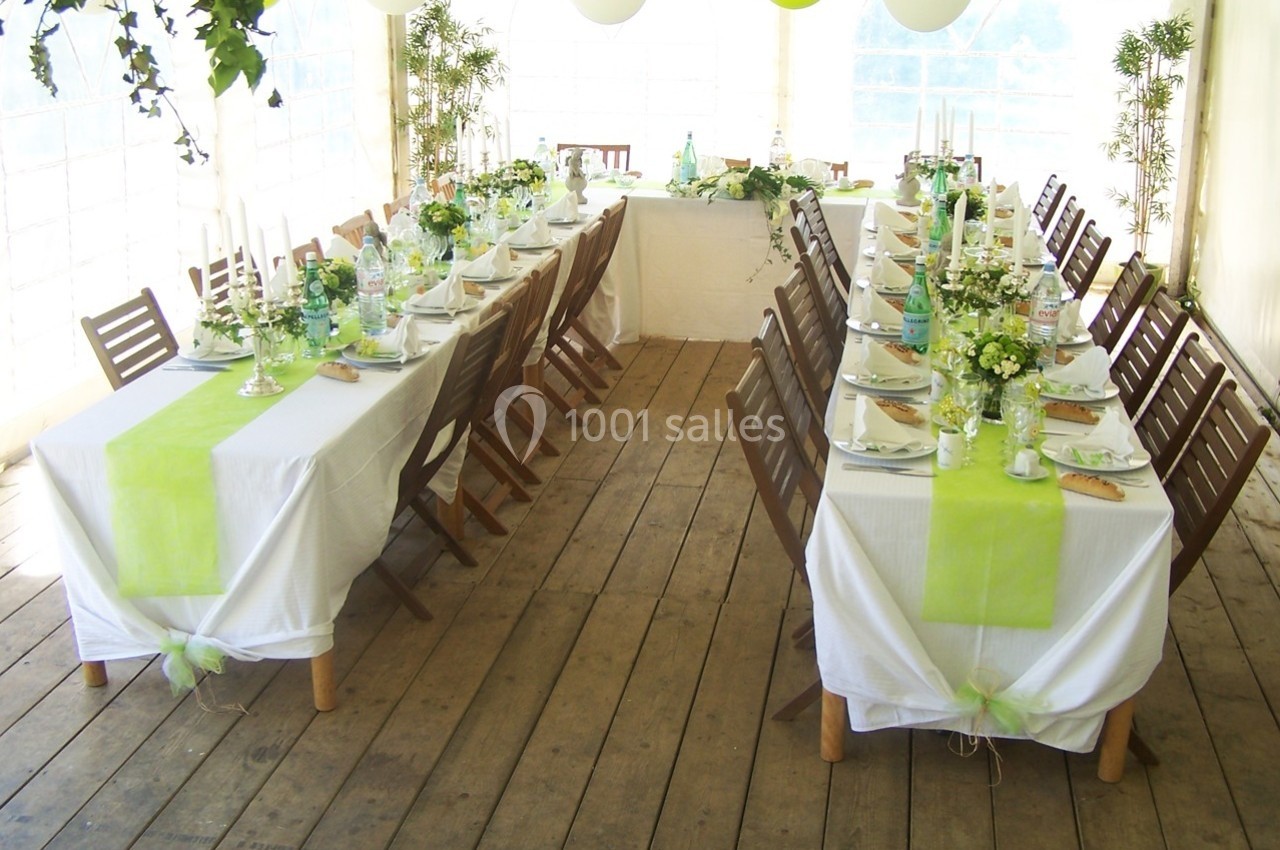 Tables décorées avec nappes blanches et chemins de table verts, disposées pour un repas dans une salle lumineuse.