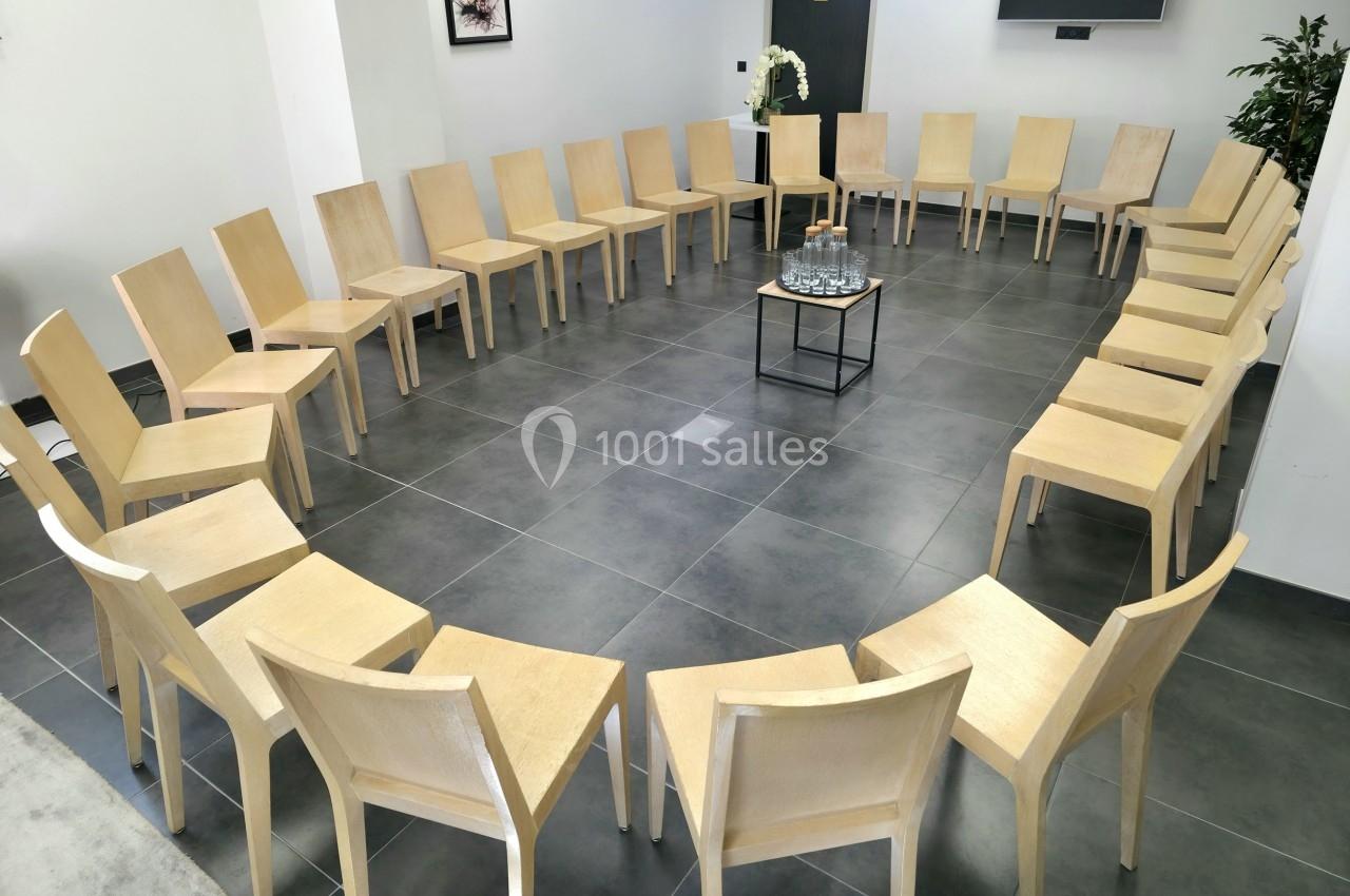 Chaises en bois disposées en cercle dans une salle lumineuse avec une table basse au centre portant des verres et une carafe.