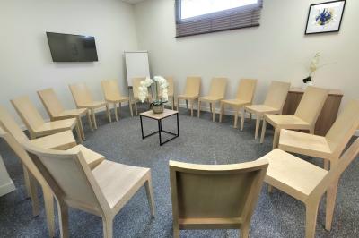 Salle de réunion avec des chaises disposées en cercle, une table basse au centre et un écran mural.
