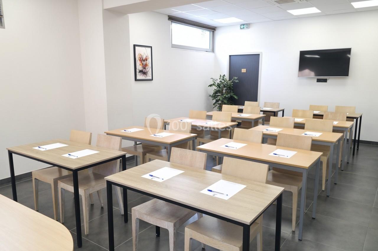 Salle de formation lumineuse avec des tables en bois, des chaises alignées, des blocs-notes et un écran mural.