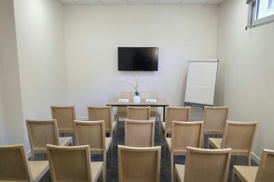 Salle de réunion avec des chaises disposées en cercle, une table basse au centre et un écran mural.