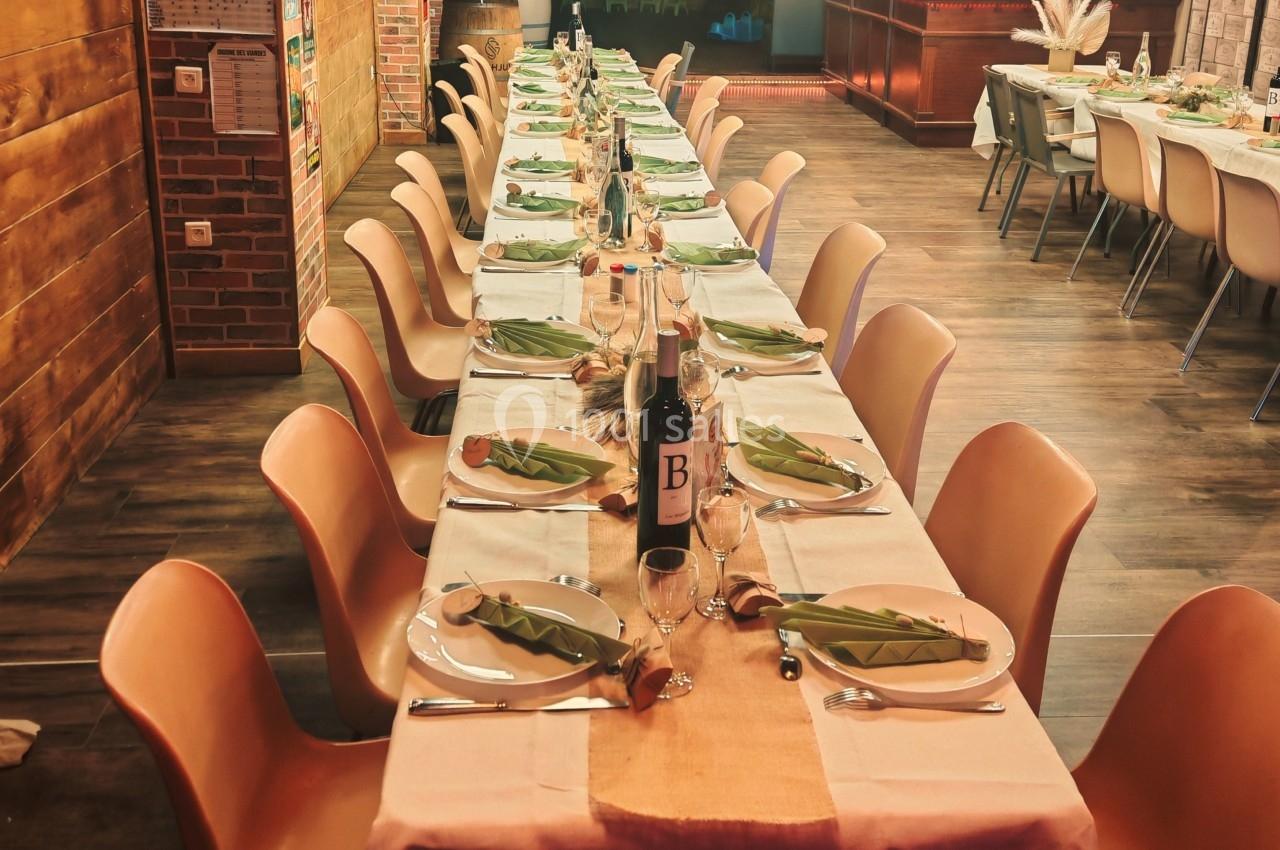 Table dressée pour un repas, avec nappes, assiettes, verres et décorations, dans une salle chaleureuse au style rustique.