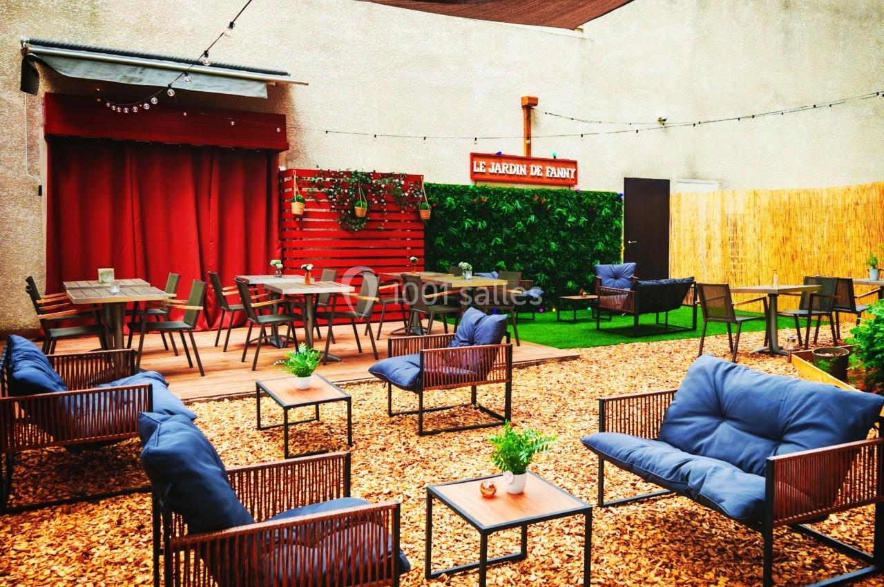 Cour extérieure aménagée avec des tables, des chaises et des fauteuils, entourée de murs et décorée de plantes vertes.