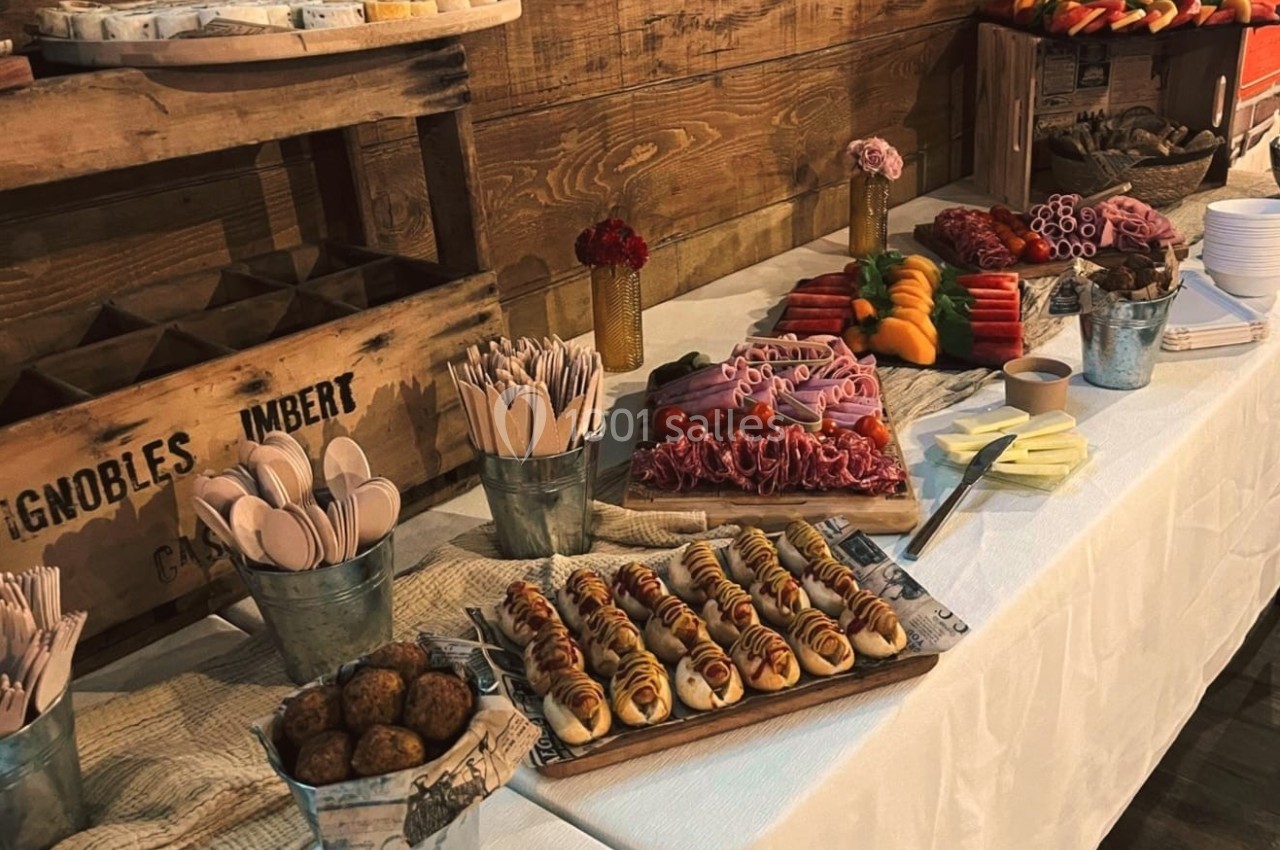 Buffet avec assortiment de charcuteries, pains, légumes, et couverts en bois sur une table décorée de seaux métalliques.