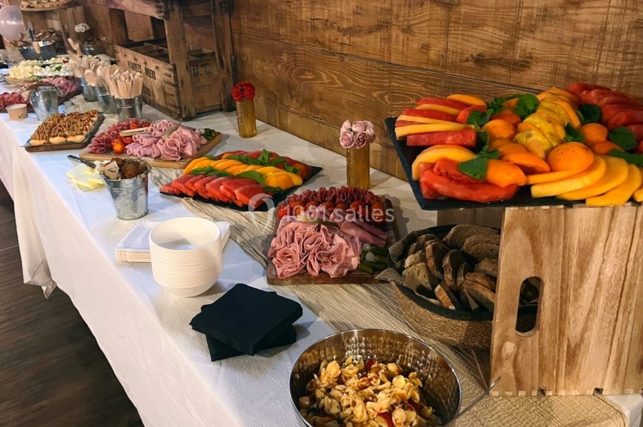 Buffet avec fruits frais, charcuterie, pain, salade de pâtes et desserts, présenté sur une table blanche en intérieur.