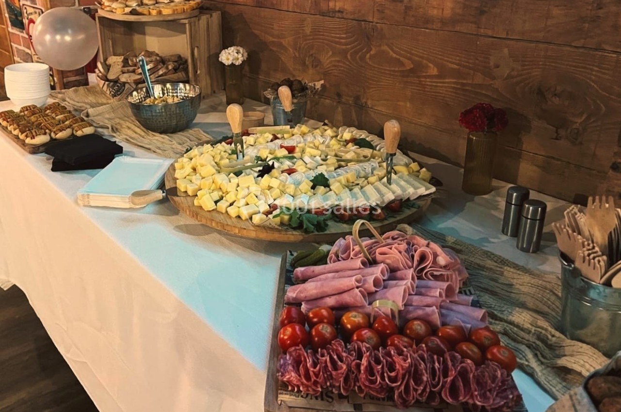 Plateau de charcuterie, fromages et légumes sur une table décorée pour un buffet, avec couverts en bois à proximité.