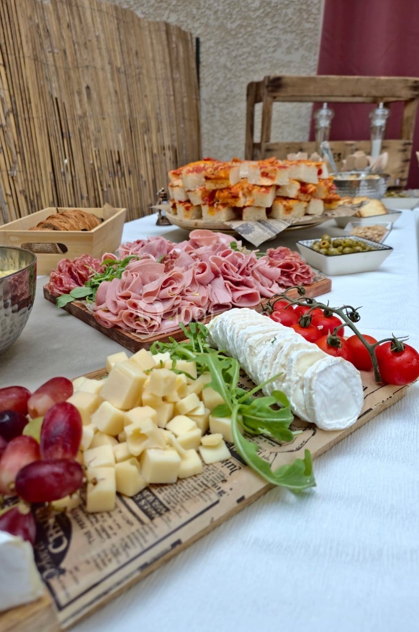 Plateau de charcuterie, fromages, tomates cerises et raisins, disposé sur une table avec d'autres mets en arrière-plan.
