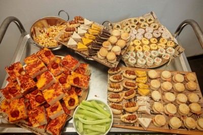 Table garnie de verrines, brochettes de fruits frais et plateaux de donuts colorés sur une nappe décorative.