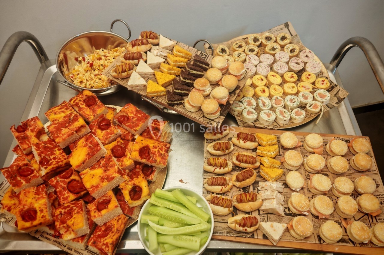 Plateau varié de snacks salés comprenant pizzas, sandwichs, mini-burgers, roulés et légumes frais.
