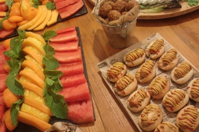 Table garnie de verrines, brochettes de fruits frais et plateaux de donuts colorés sur une nappe décorative.