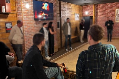 Des personnes discutent dans un espace intérieur avec des murs en briques, un écran affichant une cheminée et une ambiance…