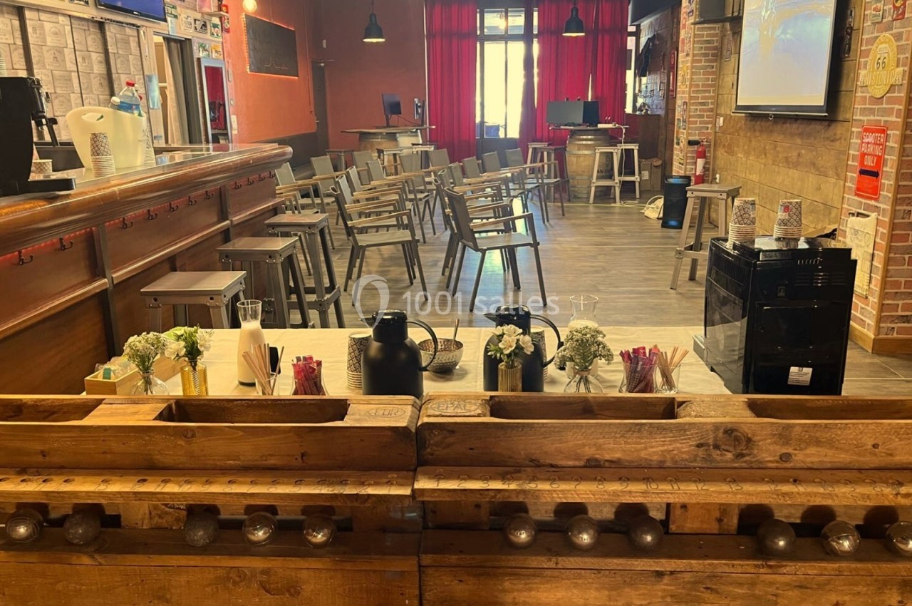 Salle aménagée avec des tables et des chaises, un bar en bois au premier plan et une ambiance chaleureuse.