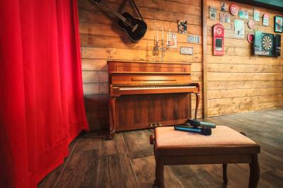 Piano en bois contre un mur décoré de cadres et d'une guitare, avec un tabouret et un micro au premier plan.
