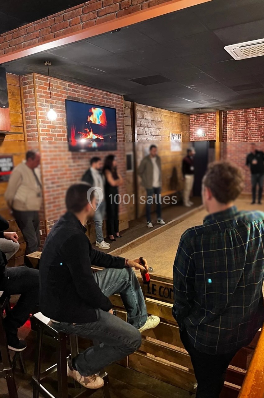 Des personnes discutent dans un espace intérieur chaleureux avec murs en briques et écran affichant une cheminée.