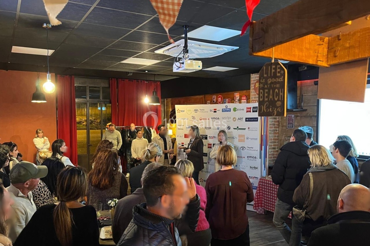 Groupe de personnes rassemblées dans une salle pour un événement, avec une présentation devant un écran et un panneau…