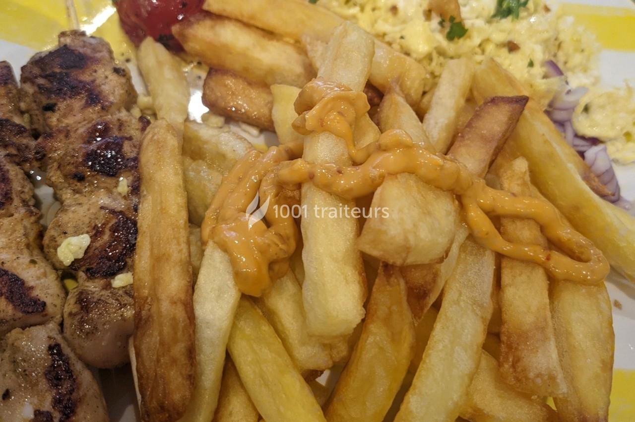 Assiette contenant des frites garnies de sauce, une brochette de viande grillée et un accompagnement d'œufs brouillés.