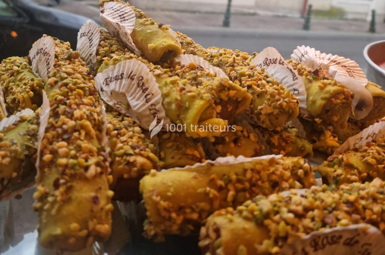 Cannoli garnis de crème, enrobés de pistaches concassées, exposés sur un plateau dans une vitrine.