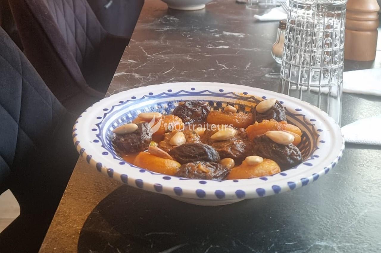 Assiette en céramique contenant un tajine sucré avec des pruneaux, abricots secs et amandes, posée sur une table sombre.